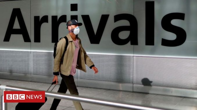 A man wearing a mask pulls his suitcase through an airport